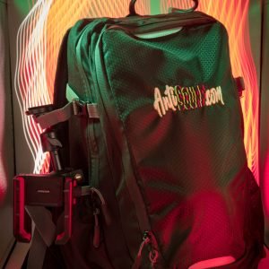 a stylish photo of the AntiScuff® IRL Backpack for Streamers. Front view, with the tripod and chat phone holder on the left side of the backpack. Behind the backpack you see strokes of light generated by slow shuttertimes of the camera that took the photo.
